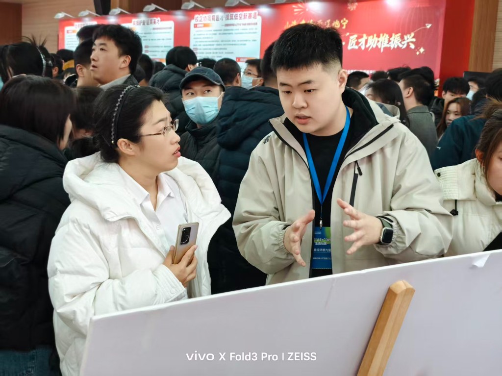 韩世禹佩戴沈阳 AI+OPC 生态社区证件，在展位向参观者讲解社区与 OPC