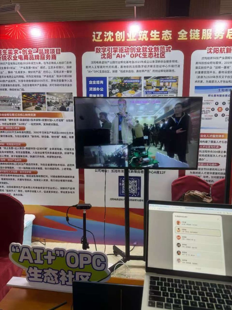 展位：立式大屏展示社区成员 AI 中医按摩 demo，前方笔记本为韩世禹举手机拍摄大屏时的界面，屏幕为小O智能体